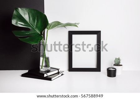 Stylish feminine space with monstera leaves in vase, cactus, notebooks, candle at home or studio with white and black background on shelf. Isolated mockup frame. Styled minimalistic still life