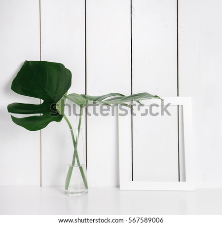 Stylish feminine space with candle, wooden box, jewellery and monstera leaves in vase at home or studio with white wooden background on shelf. Isolated mockup frame. Styled still life