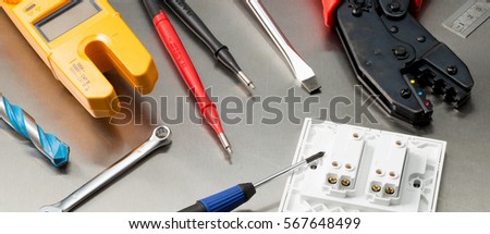 Various electrician tools and components including a multimeter, screwdrivers, wirecutters, drill bits, switches and sockets. Web banner format. Royalty-Free Stock Photo #567648499