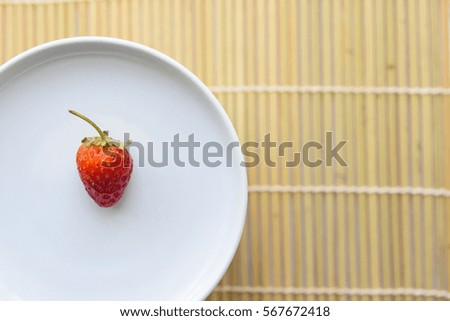Single fresh strawberry on the white dish,Wooden texture background