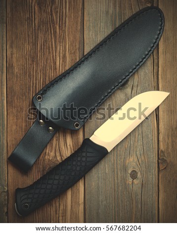 steel hunting knife near the leather sheath on an old wooden surface. instagram image filter retro style