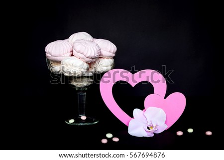 Orchid Phalaenopsis, pink hearts and marshmallows in a glass vase. Pink and white still life on black background. Valentine's day holiday.