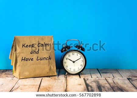 Paper bag and clock on blue background with a notes keep calm and have lunch.
