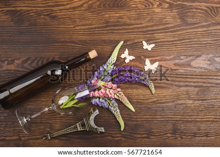 Bottle of wine and wineglass with puffy violet lupins on the wooden background
