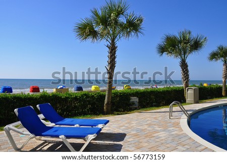 Two lounge chairs pool side with pretty beach scene in background Royalty-Free Stock Photo #56773159