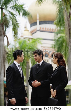 Two businessmen and one businesswoman standing, having a discussion, mosque in the background