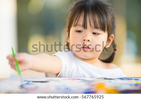 little asian girl painting with paintbrush and colorful paints