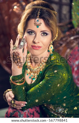 Close-up portrait of a beautiful woman in green Indian traditional dress, with her hands painted with henna mehendi.