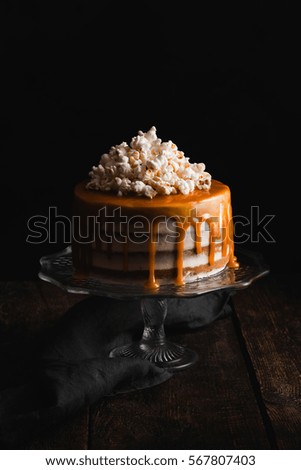 Cake with popcorn, salted caramel to stand on a wooden table on a dark background. Low key. Dark picture.