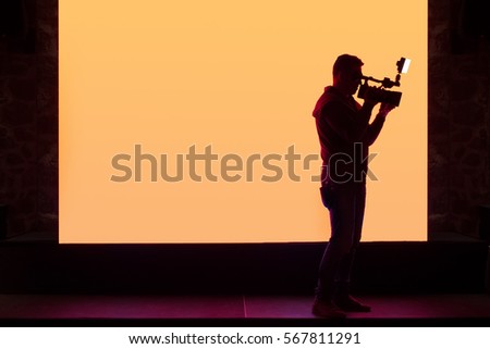 Camera operator filming in front of illuminated screen