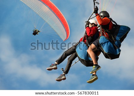 Two paraglider tandem fly against the blue sky,tandem paragliding guided by a pilot Royalty-Free Stock Photo #567830011