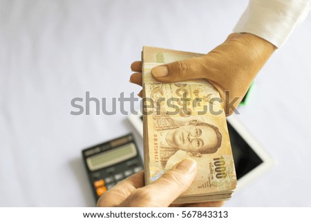 Close up 2 hands with stack of 1000 Bath Thai money on white background. BankNotes Thailand - Calculator and tablet