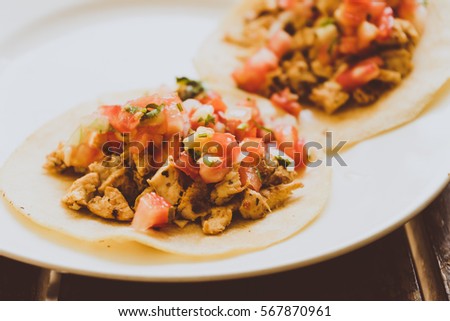 Two Mexican chicken tacos with chirmol on a white plate.