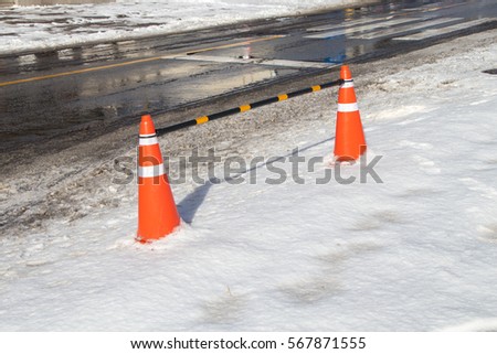 Bright orange traffic cones standing over snow after a blizzard.orange traffic cone in winter covered with snow.Snow storm brings on hazardous road conditions. 