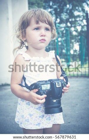Little girl holding a camera and taking pictures. Little baby girl professional photographer outdoors. Concept development and training success.