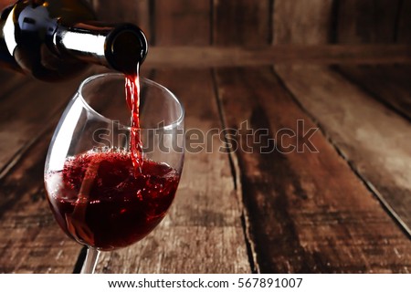 Red wine in glass on wooden background. Beautiful alcohol background. Red wine pouring from bottle. Free space for text on wooden backdrop. Royalty-Free Stock Photo #567891007