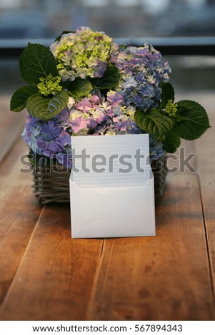 Basket with blue hydrangeas and greeting envelope on a wooden background. Holiday card.