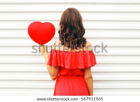 Woman back in red dress with air balloons heart shape over white background