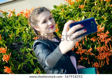 Portrait of young lady using mobile phone taking selfie on outdoor background
