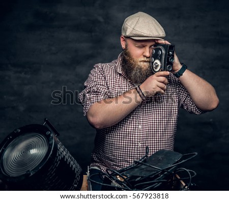 The fat bearded hipster male holds vintage 8 mm video camera and colorful soffits lamps.