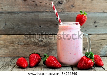 Healthy strawberry smoothie in a mason a jar glass with scattered berries over a rustic wood background Royalty-Free Stock Photo #567945451