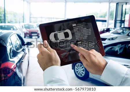 Businessman using digital tablet next to smartphone against view of row new car