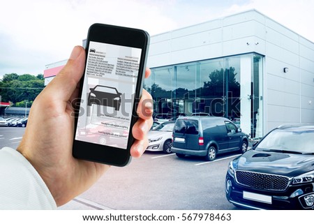 hand holding smartphone against outside view of car dealership