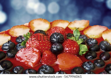 Picture of jelly cake topped with slice strawberry and fresh blueberry against light bokeh background