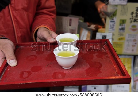 In the picture we can see a man holding a tray with two cups to serve hot green tea. Green tea is very popular in Japan.