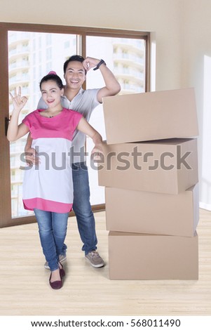 Full length of beautiful woman and man showing ok sign while standing besides stack of boxes 