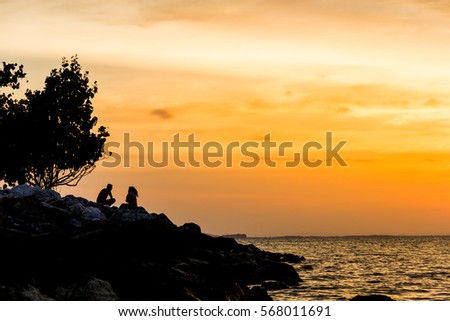 men and women relax sitting on rock beach with silhouette and colorful sky background