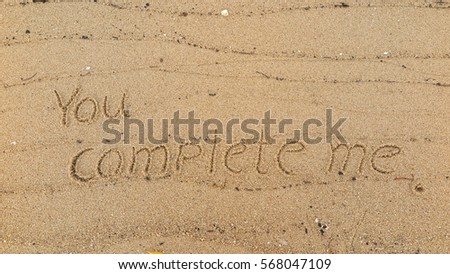 Handwriting words "You complete me." on sand of beach