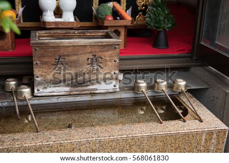 In the picture we can see a photo of a monastery where holy water is stored and some wooden handle spoons are kept on the top of the water reservoir.