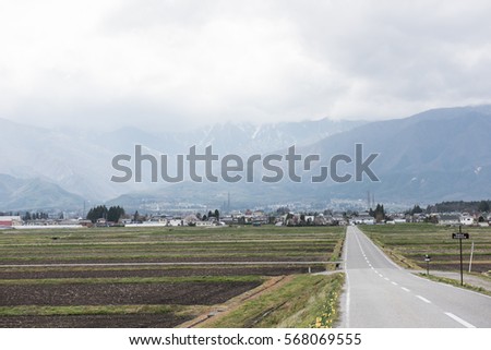 The picture shows an agricultural land and a long and empty road leading to the mountains.