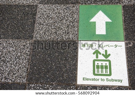 In the picture we can see a road sign showing direction to the elevator. The tiles of the road is very attractive which can be seen on the background of the picture.
