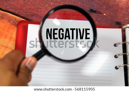 A concept image of a magnifying glass zoom on a notebook over a wood background  with a word NEGATIVE zoom inside the glass 