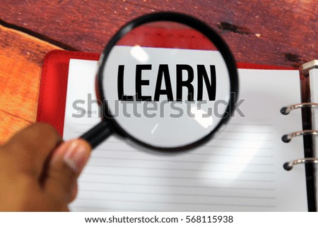 A concept image of a magnifying glass zoom on a notebook over a wood background  with a word LEARN zoom inside the glass 