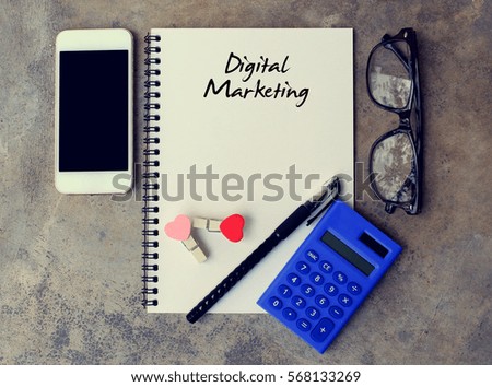 Digital Marketing - text on notebook. smartphone,calculator, pen, glasses on the desk. top view.