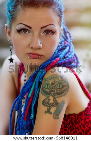 Cool young punk girl with braided blue hair and facial piercing posing for a photo. Portrait of a diverse female model with a tattoo and makeup