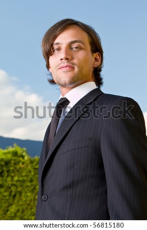 Young businessman with longer hair over a blue sky outside.