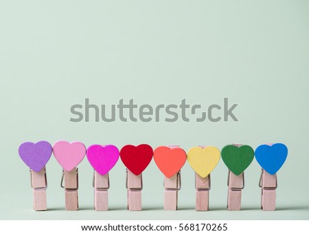 Colored heart shaped clothespins in row on greenery background
