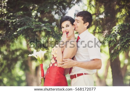 Groom with red tie hugs bride in red wedding dress.