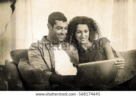 Grey background against young couple using laptop while sitting on sofa