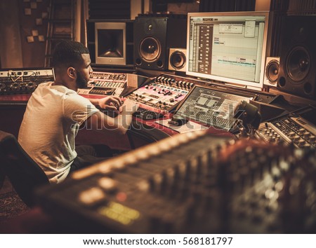 African american sound engineer working at mixing panel in boutique recording studio. Royalty-Free Stock Photo #568181797