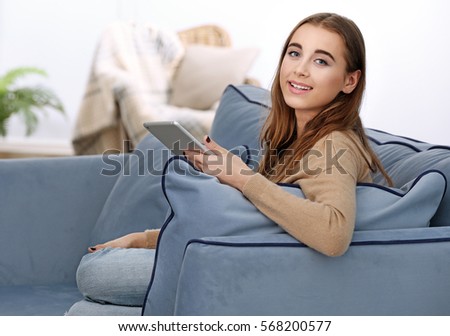 Pretty teenager girl with tablet sitting on couch