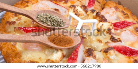 Close up of delicious seafood Hawaiian Italian pizza in delivery box with oregano and chill pepper in spoon.