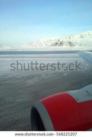 The winter landscape with the aerodrome, mountains and the fragment of the red airplane. This mobile photo was taken through the window of the airplane in Svalbard Airport in Longyear, Svalbard.   