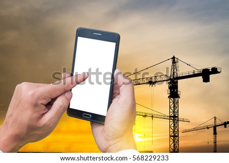 The human hands holding the smartphone and touch on mobile screen with silhouette crane and construction site