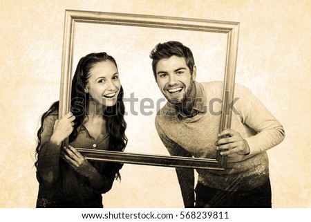 Portrait of happy couple holding picture frame against grey background