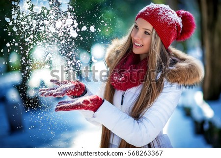 Winter portrait of young beautiful blond woman wearing knitted snood covered in snow. Snowing winter beauty fashion concept.